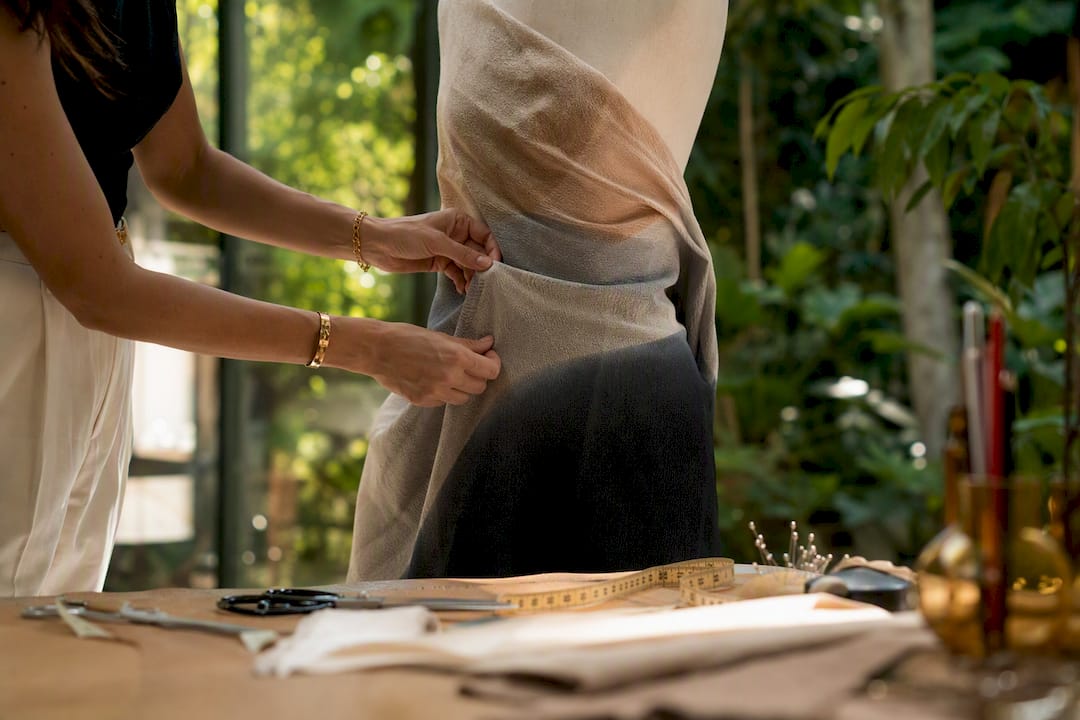 Hands adjusting dress form with fabric for sizing