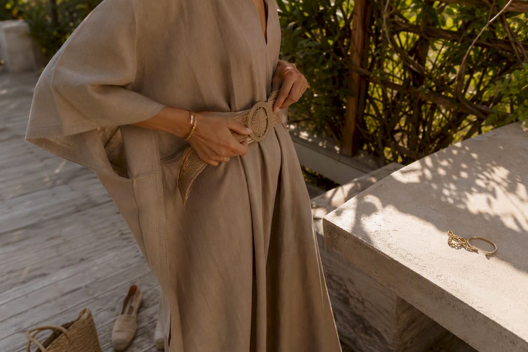 Woman adjusting belt on kaftan near shoes and bag
